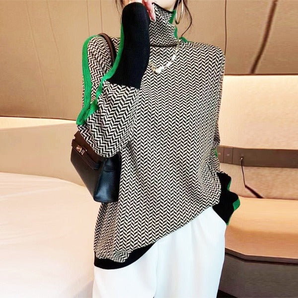 Femme portant le pull à chevrons noir et blanc avec liserés verts, col montant, pantalon blanc et petit sac noir. 2