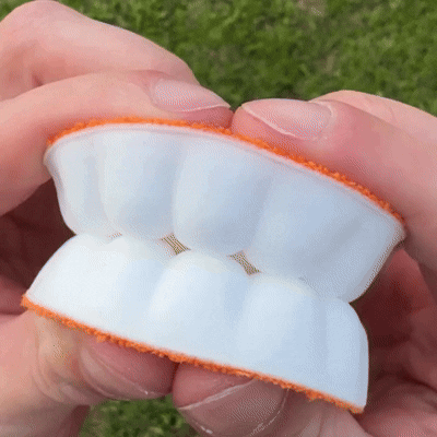 Gros plan en extérieur sur une semelle pliée entre les doigts, montrant la mousse blanche alvéolée et le tissu orange. 18