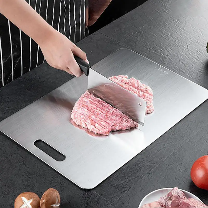 Personne en tablier rayé qui hache de la viande à l'aide d'un couperet sur la planche en inox posée sur un plan sombre. 6