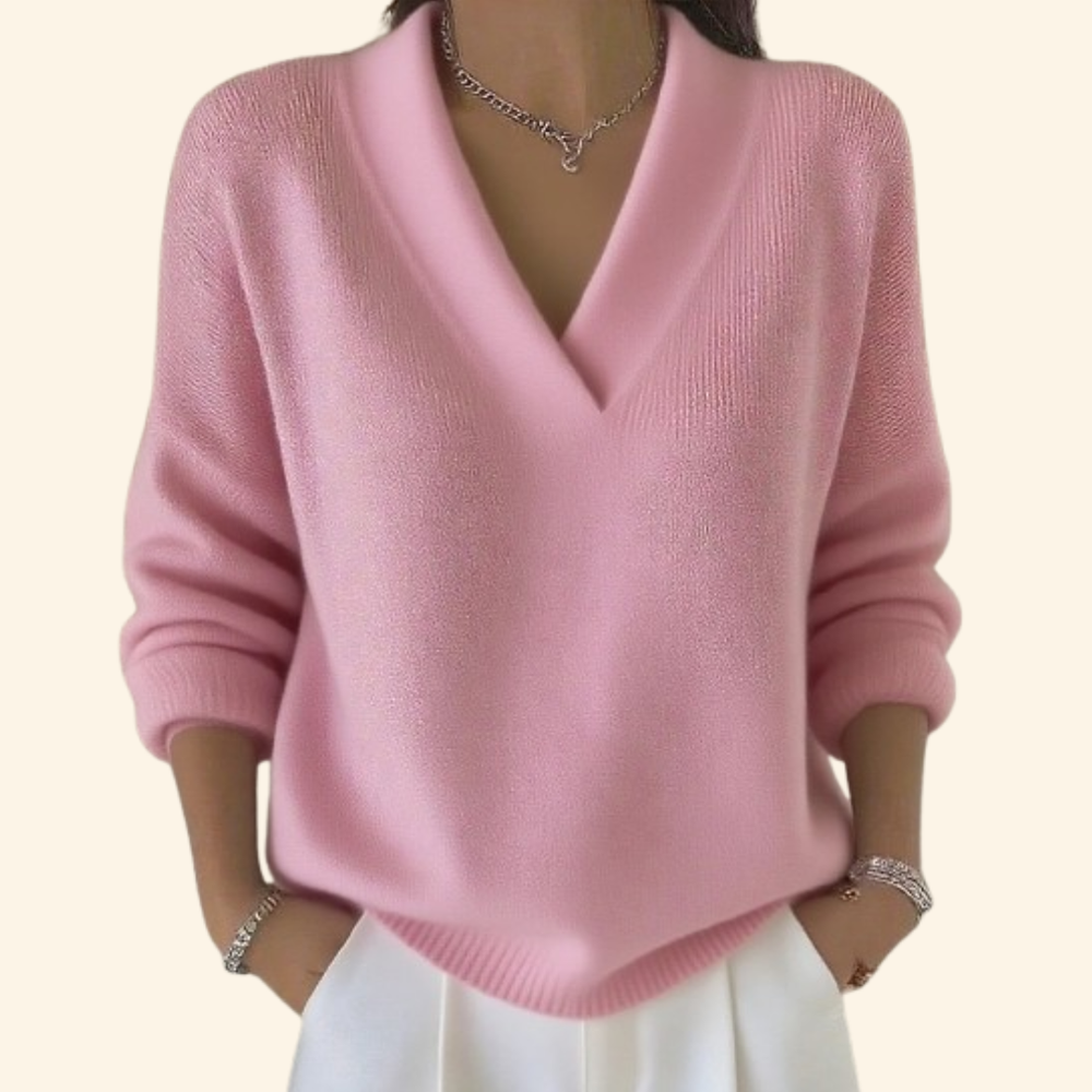 Pull rose clair à col en V et manches longues, porté avec un pantalon blanc, mains dans les poches. 2