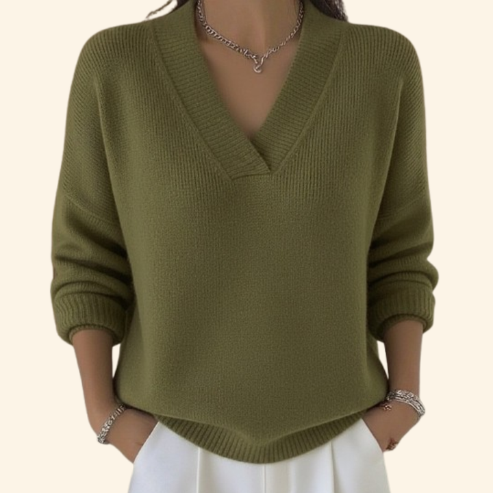 Pull vert olive en maille côtelée à col en V, porté avec un pantalon blanc et un collier argenté. 3