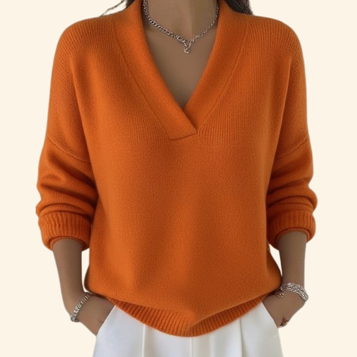 Pull orange en maille à col en V ample, porté avec un pantalon blanc, mains dans les poches. 5