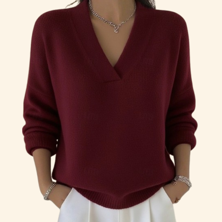 Pull bordeaux en maille à col en V, porté par une femme avec pantalon blanc et bijoux argentés. 1