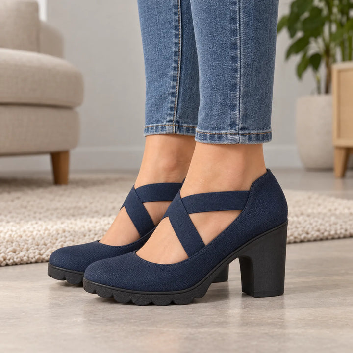 Femme en jean portant les chaussures bleu marine à bride élastique croisée et talon bloc, vues de côté dans un salon. 2