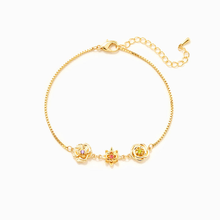 Bracelet doré à chaîne fine avec trois fleurs ornées d'une petite pierre colorée, fermoir mousqueton et chaînette de rallonge, vu à plat. 1