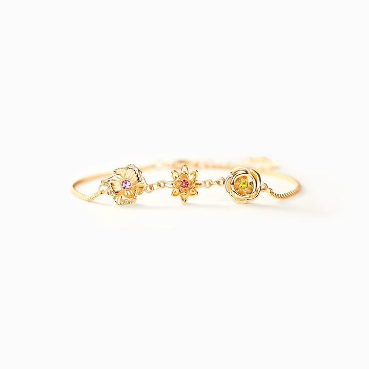 Bracelet doré vu de face et de près, posé sur fond clair, avec ses trois fleurs serties de pierres violette, rouge et verte. 4