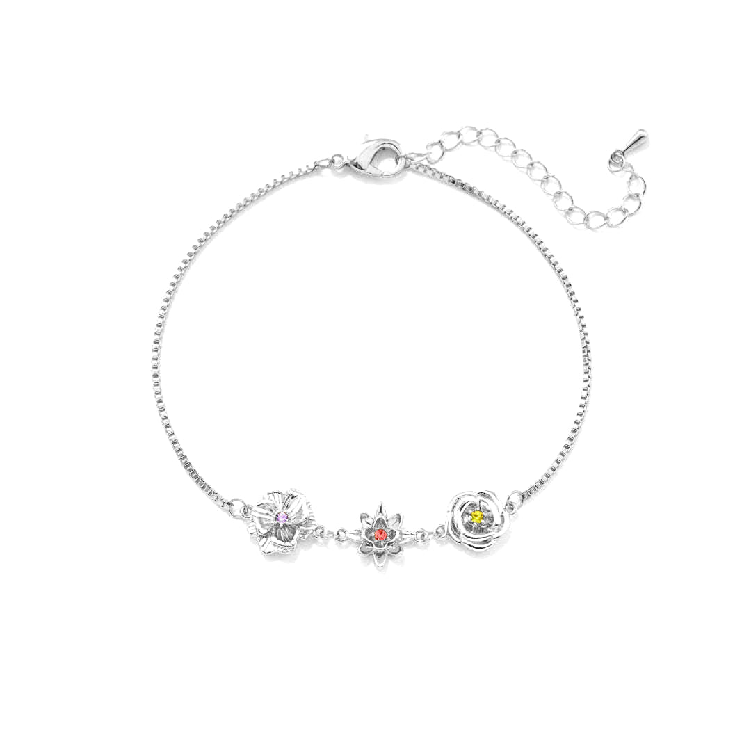 Version argentée du bracelet, vue à plat sur fond blanc : trois fleurs serties d'une pierre colorée et chaînette de rallonge. 2