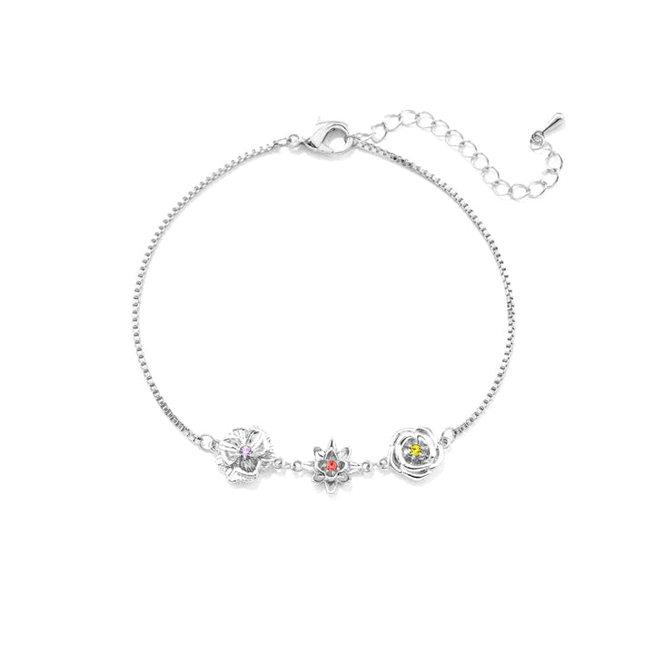 Version argentée du bracelet, vue à plat sur fond blanc : trois fleurs serties d'une pierre colorée et chaînette de rallonge. 2