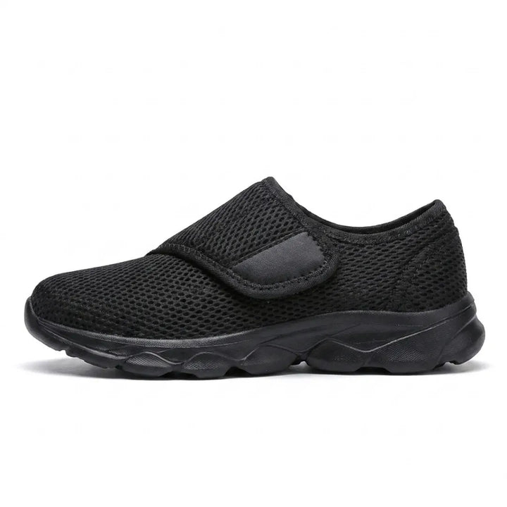 Vue de profil de la chaussure entièrement noire en mesh aéré, sangle auto-agrippante et semelle noire. 10