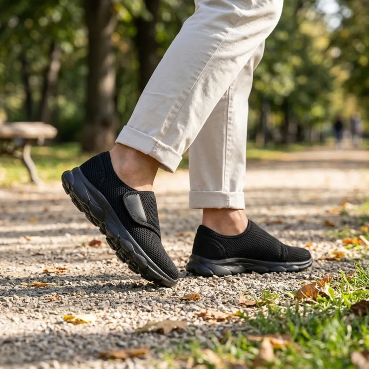 Pieds d'un marcheur portant les chaussures noires à sangle, pantalon beige retroussé, sur un chemin de gravier dans un parc. 11