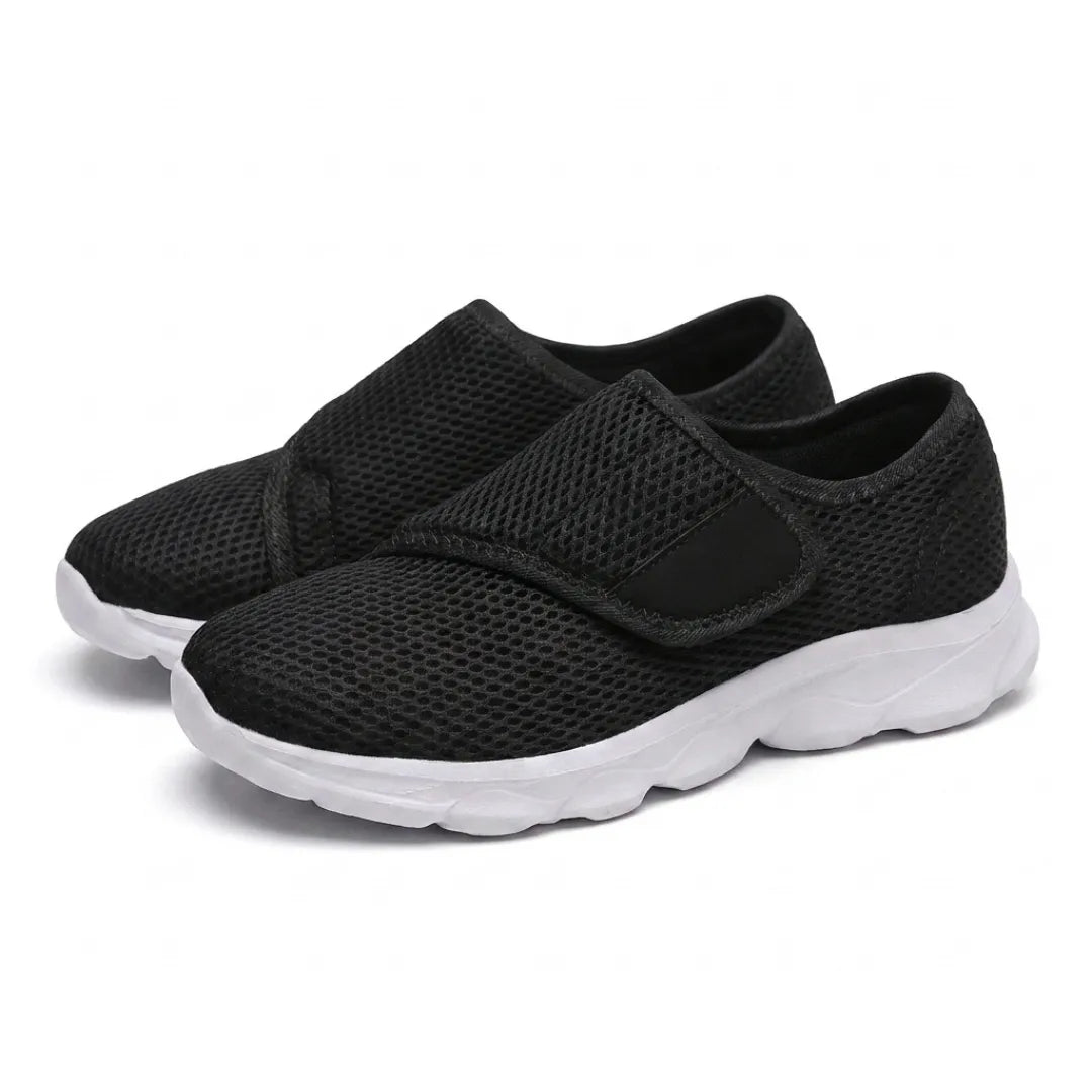 Paire de chaussures noires en mesh aérée, sangle auto-agrippante sur le dessus et semelle blanche épaisse, vue de trois quarts sur fond blanc. 25