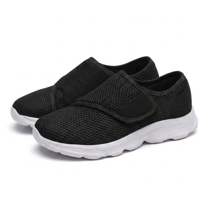 Paire de chaussures noires en mesh aérée, sangle auto-agrippante sur le dessus et semelle blanche épaisse, vue de trois quarts sur fond blanc. 25