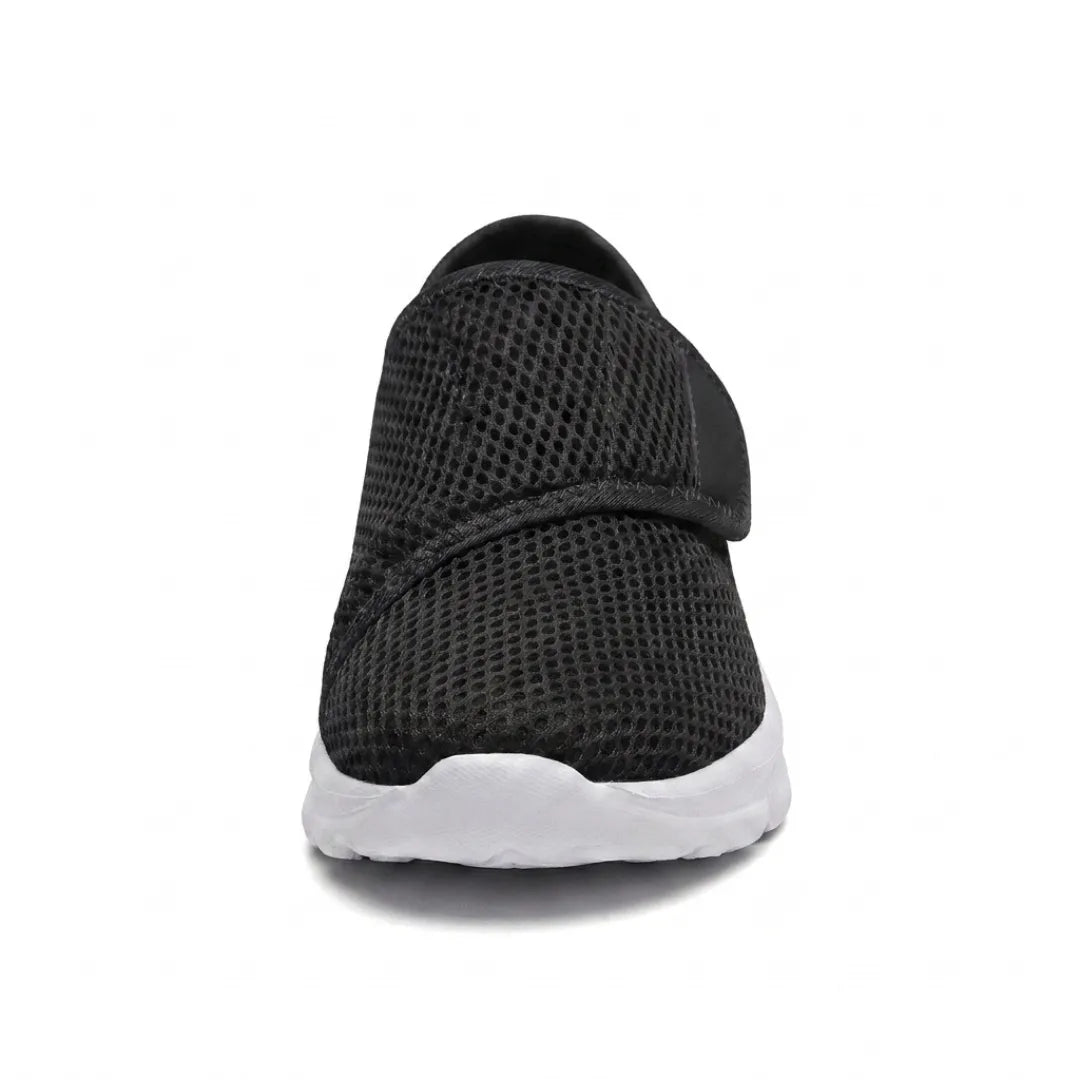 Vue de face d'une chaussure noire en mesh avec sangle auto-agrippante, montrant la largeur de l'empeigne et la semelle blanche. 26