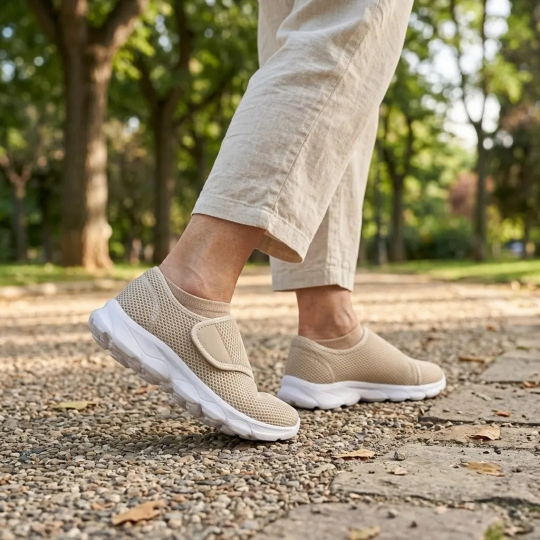 Pieds d'une personne marchant sur un chemin de gravier dans un parc, chaussés de modèles beiges en mesh, pantalon de lin clair. 29