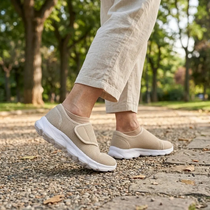 Pieds d'une personne marchant sur un chemin de gravier dans un parc, chaussés de modèles beiges en mesh, pantalon de lin clair. 29