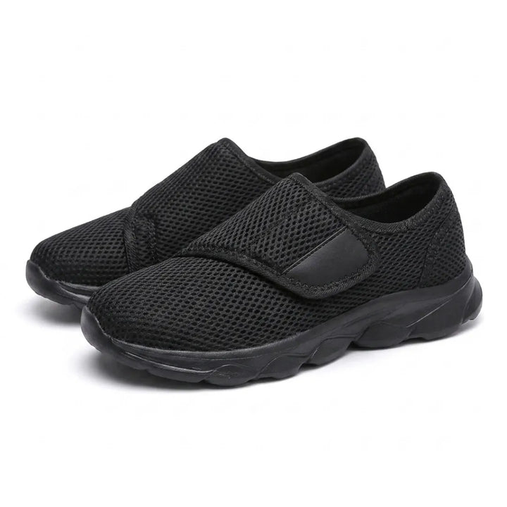 Paire de chaussures toutes noires en mesh aéré à sangle auto-agrippante, vue trois-quarts sur fond blanc. 16