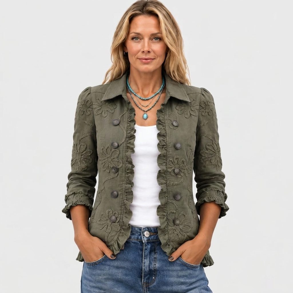 Vue de face, la veste kaki à fleurs brodées portée ouverte sur un top blanc, avec un collier turquoise et les mains dans les poches. 2