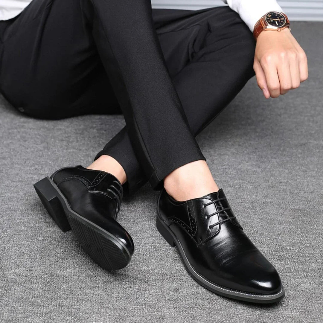 Homme assis en pantalon noir portant les chaussures noires, jambes croisées, montrant la semelle crantée et les lacets. 4