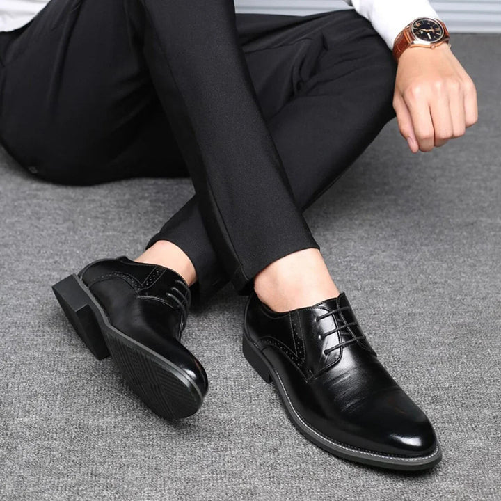 Homme assis en pantalon noir portant les chaussures noires, jambes croisées, montrant la semelle crantée et les lacets. 4