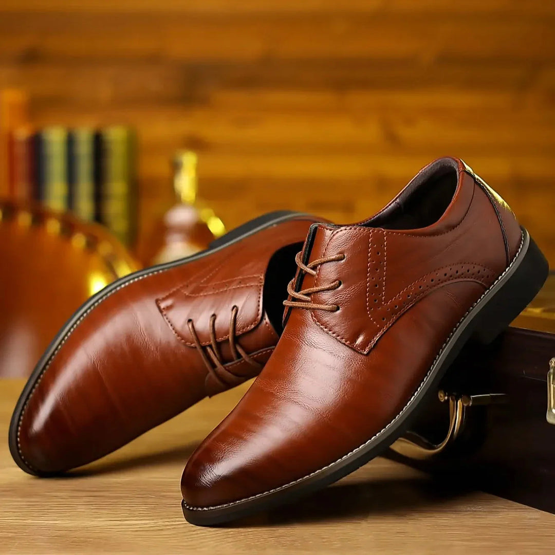 Paire de chaussures à lacets en cuir brun cognac brillant, posées en biais sur une table en bois dans un décor chaleureux. 1