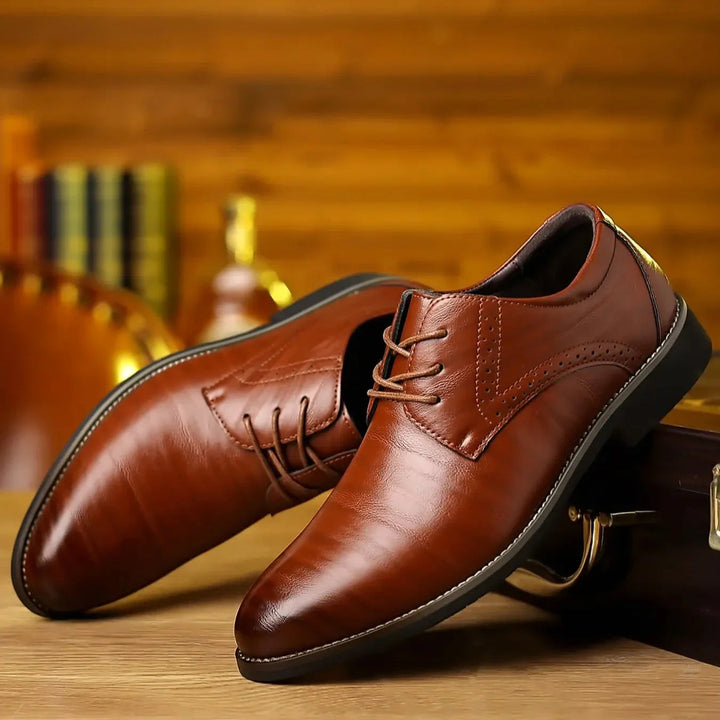 Paire de chaussures à lacets en cuir brun cognac brillant, posées en biais sur une table en bois dans un décor chaleureux. 1