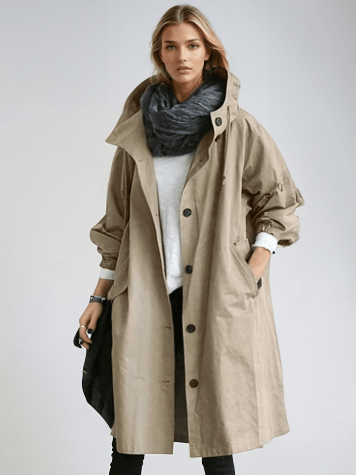 Femme portant le trench à capuche beige boutonné, col montant, écharpe grise et haut blanc, une main dans la poche. 3