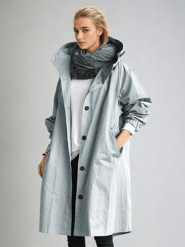 Femme en trench à capuche gris-bleu clair aux reflets brillants, porté avec écharpe grise, haut blanc et pantalon noir. 5