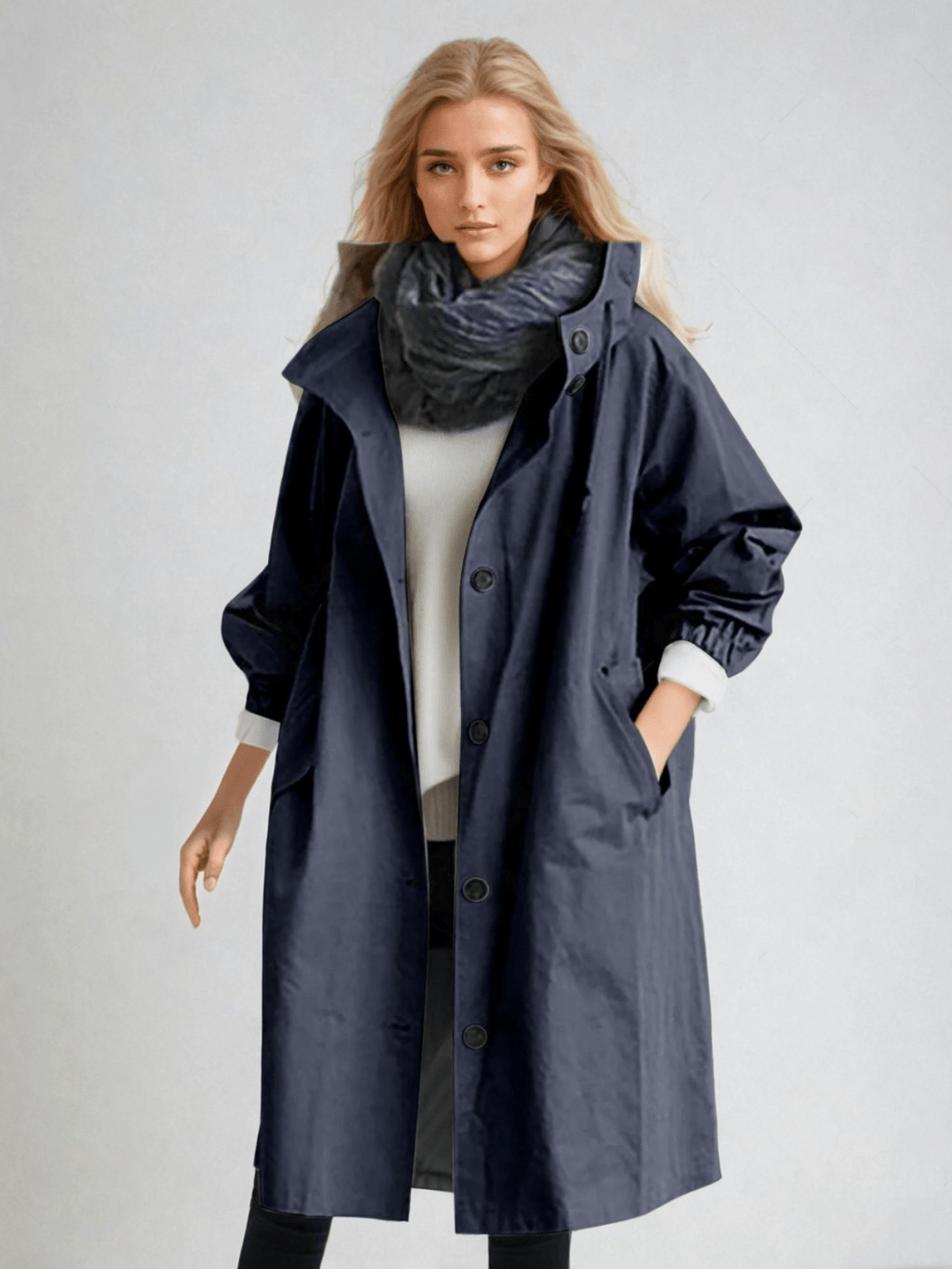 Femme portant le trench à capuche bleu marine boutonné jusqu'au col, avec écharpe sombre, pull blanc et pantalon noir. 7