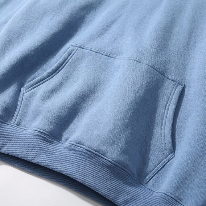 Gros plan sur la poche kangourou bleu ciel, ses surpiqûres et le bas côtelé du sweat à capuche. 4