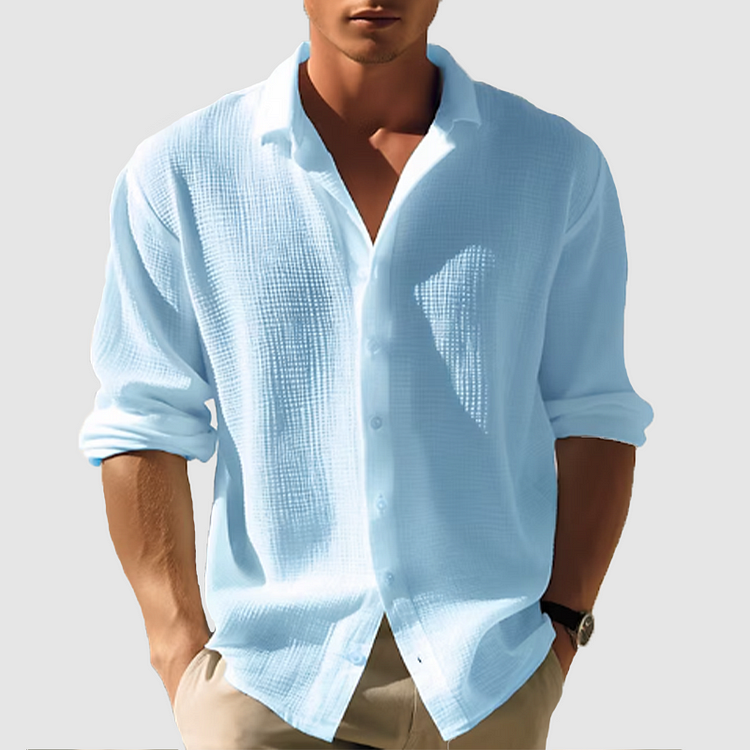 Homme portant la chemise texturée bleu ciel, manches retroussées, boutonnée devant, mains dans les poches d'un pantalon beige. 1