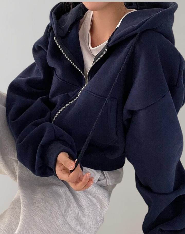 Sweat bleu marine zippé porté avec un t-shirt blanc et un pantalon gris, main tenant un cordon de capuche. 3