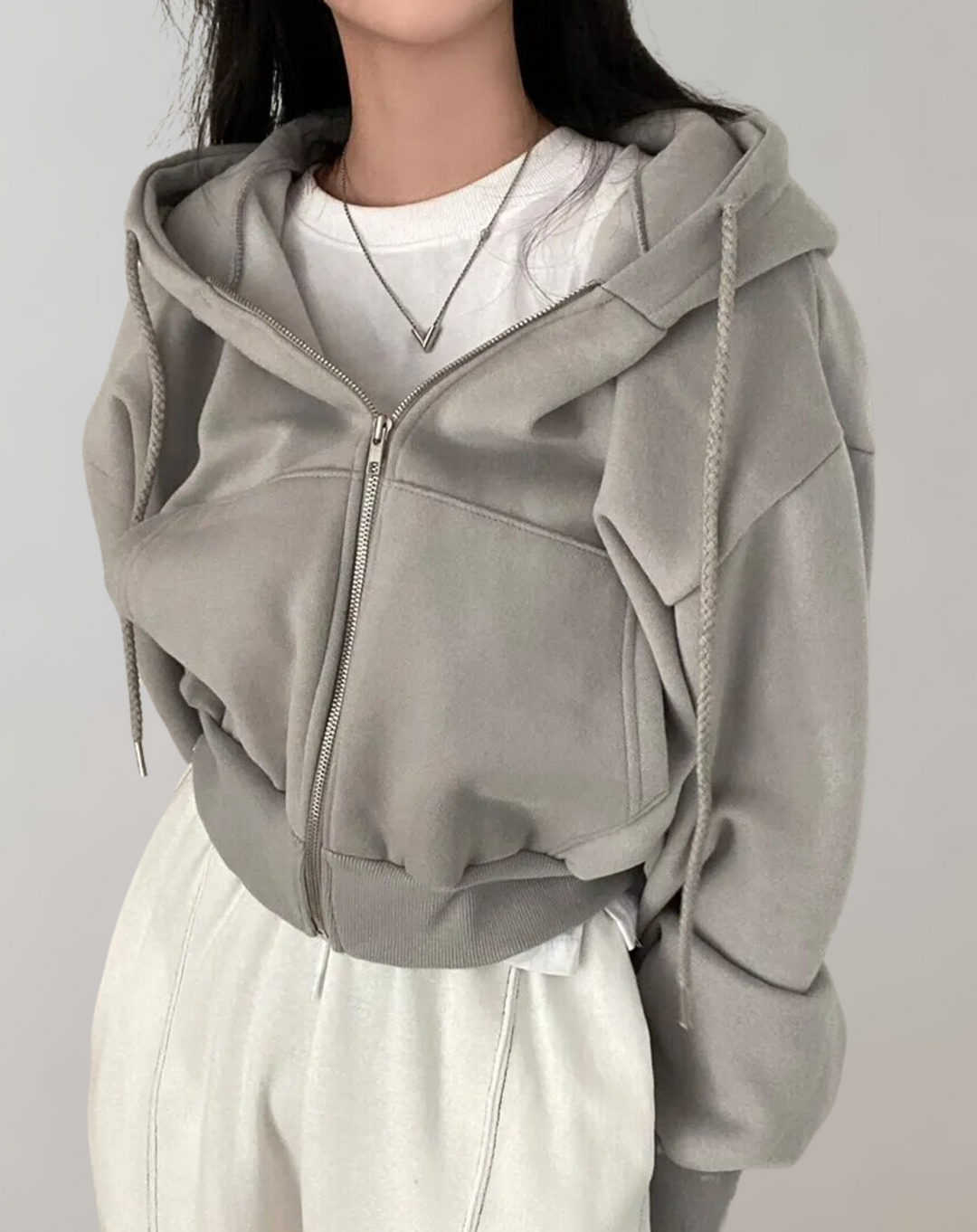 Sweat gris zippé porté en tenue citadine avec un t-shirt blanc, un collier et un pantalon blanc, bord-côtes bien visible. 4