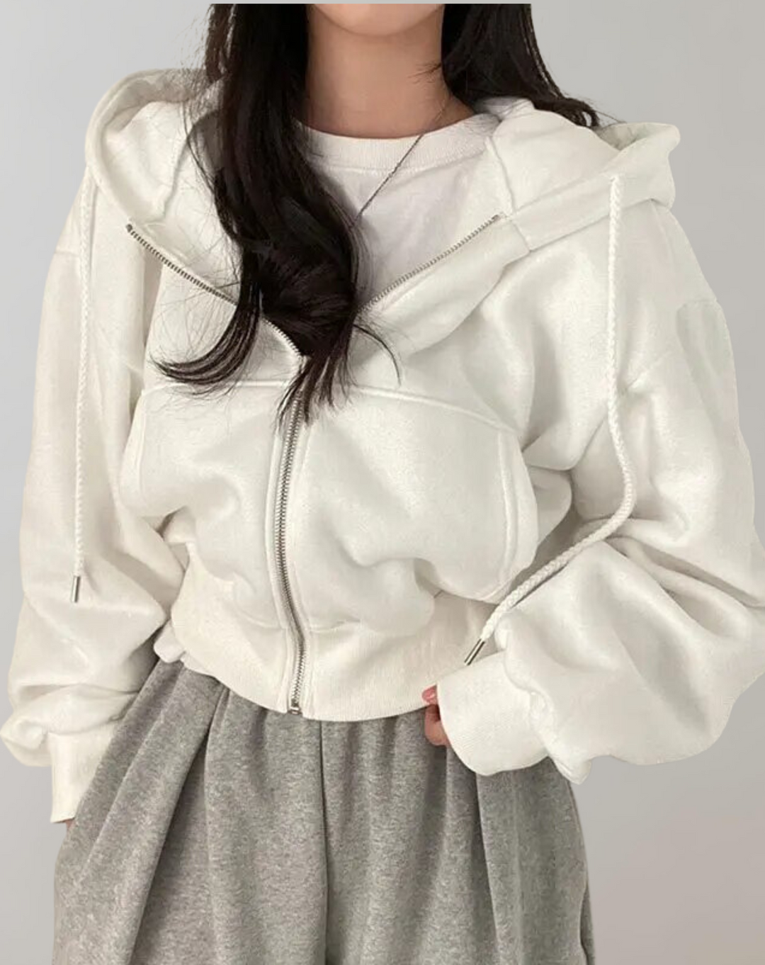Sweat blanc zippé porté par une femme avec un jogging gris, vue de face, cordons de capuche tombant sur la poitrine. 1