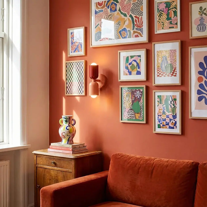 Applique rouge et corail allumée sur un mur terracotta couvert de cadres colorés, au-dessus d'une commode et d'un canapé. 5