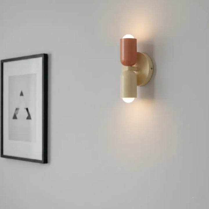 Gros plan de l'applique allumée, lumière vers le haut et le bas, tête corail et tête crème sur mur gris. 4