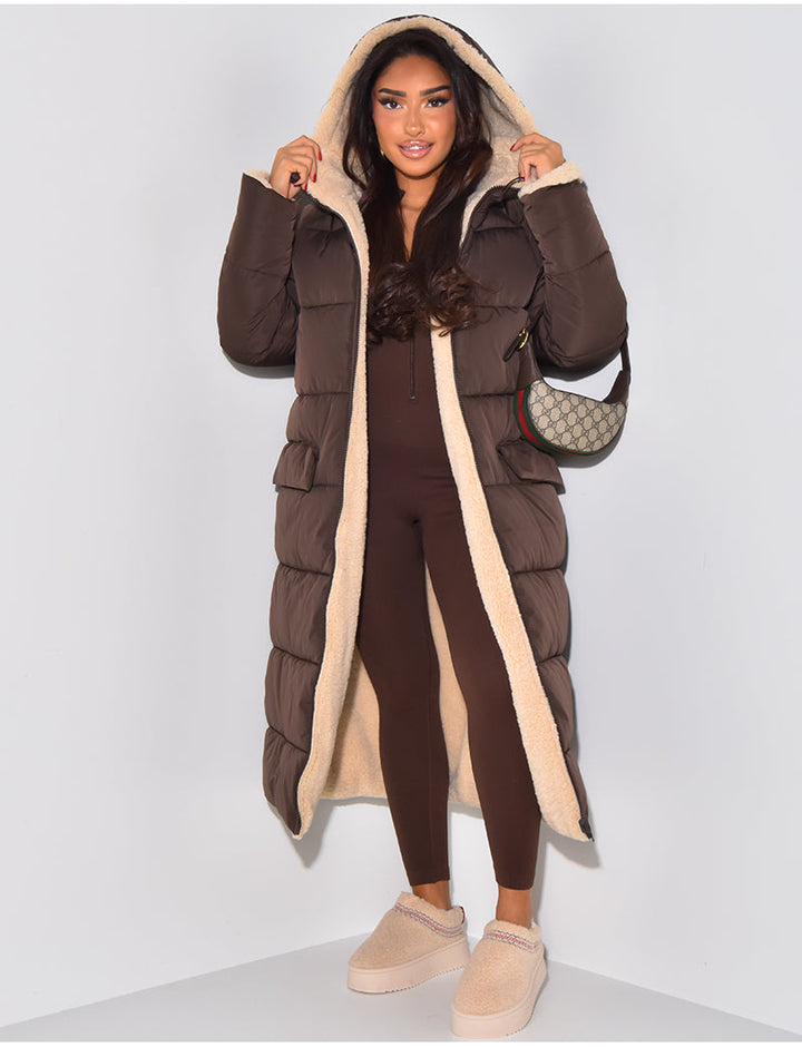 Femme portant le manteau matelassé marron ouvert, capuche relevée et doublure en fourrure beige visible, avec une combinaison marron. 2