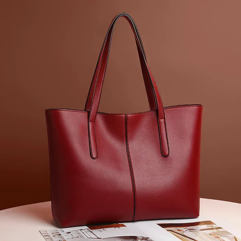 Sac cabas rouge bordeaux posé sur une table devant un mur brun, anses dressées 3