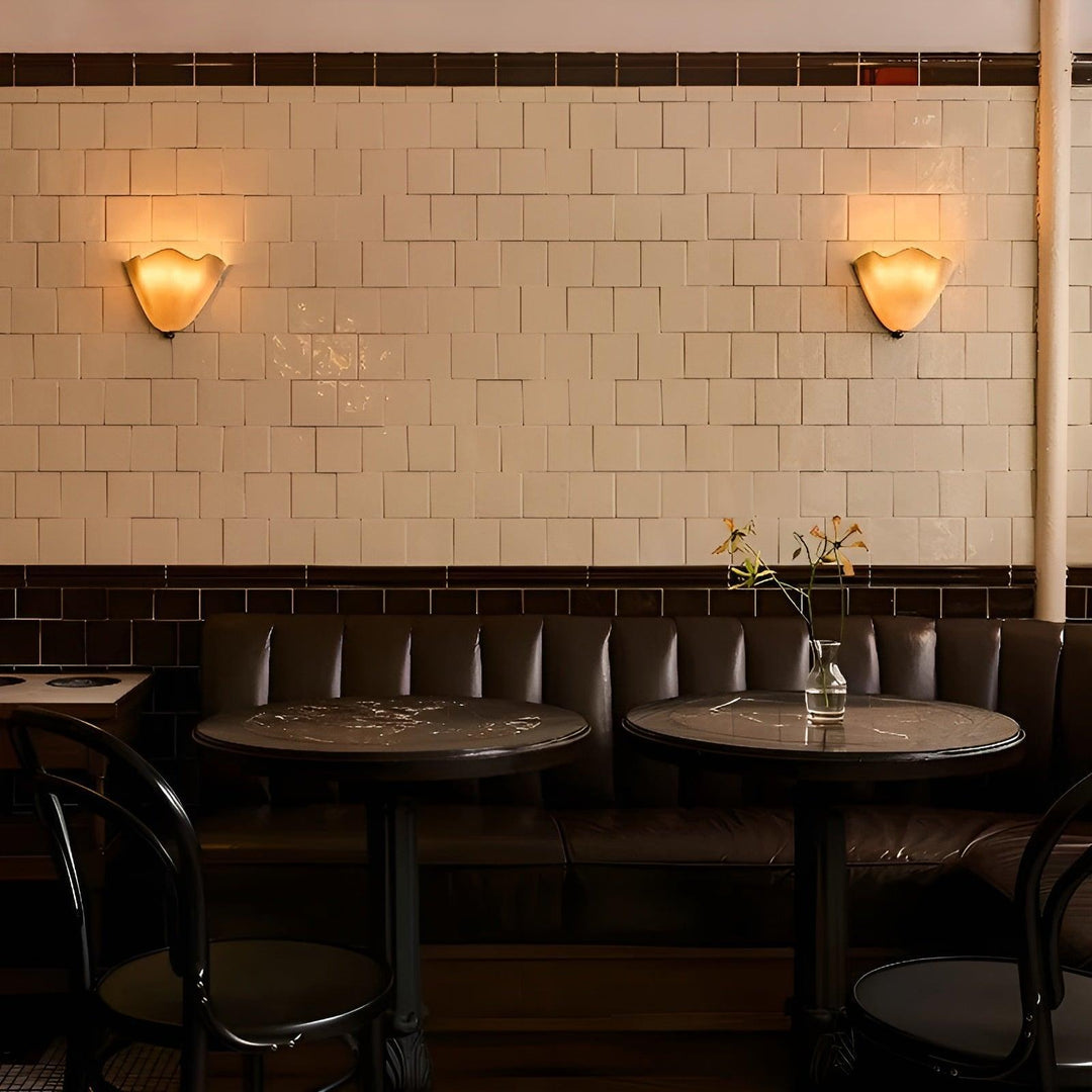 Deux appliques allumées de chaque côté d'un mur de carreaux blancs dans un café avec banquette et tables rondes. 4