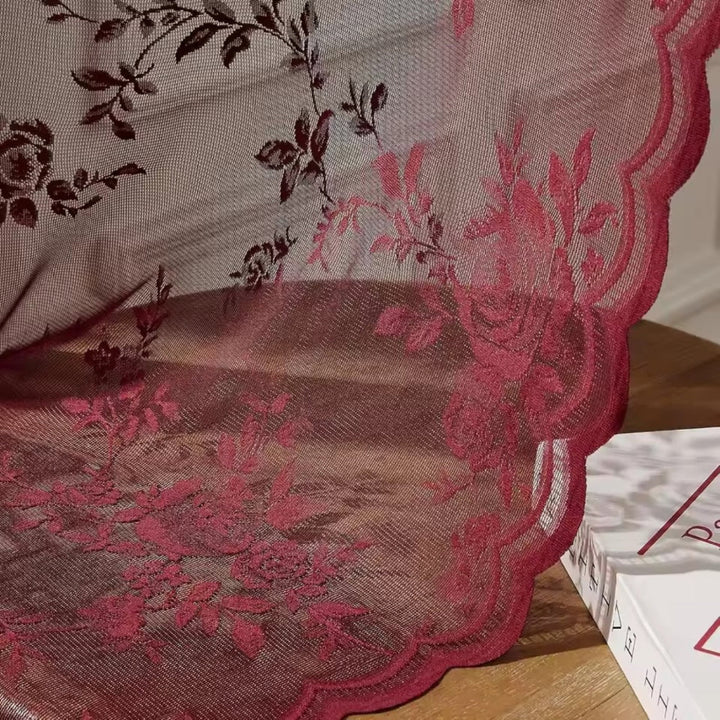 Gros plan sur la dentelle rouge bordeaux, ses roses brodées et son bord festonné, posée près d'un livre. 3