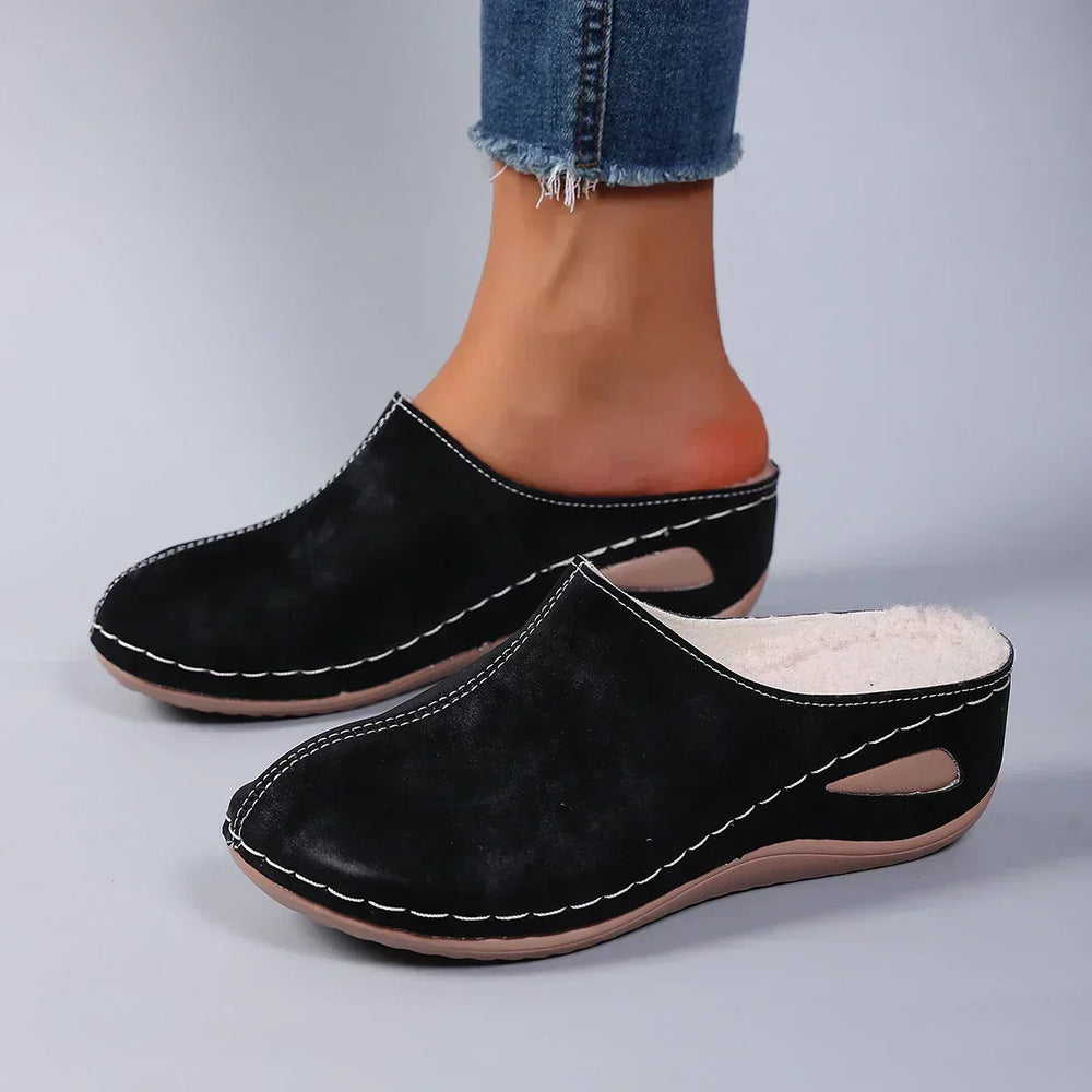 Chaussons noirs portés par une femme en jean, vue de profil montrant la doublure polaire et la semelle compensée. 2