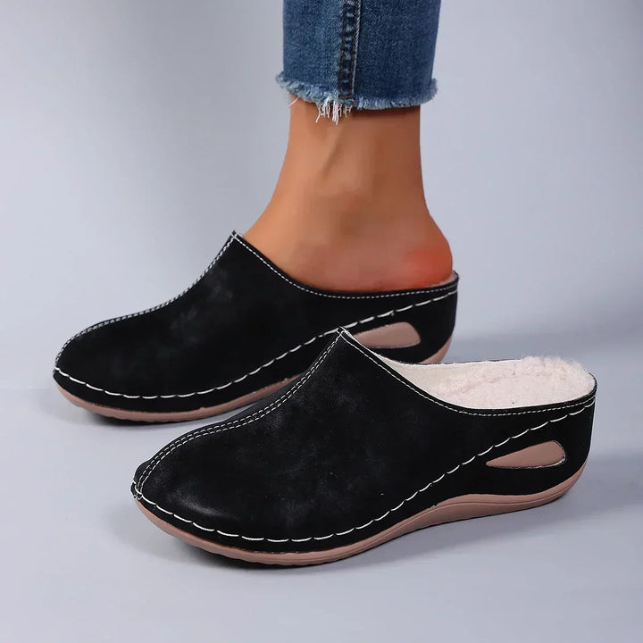 Chaussons noirs portés par une femme en jean, vue de profil montrant la doublure polaire et la semelle compensée. 2