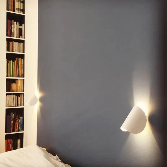 Deux appliques blanches orientables fixées sur un mur bleu-gris de chambre, à côté d'une bibliothèque remplie de livres. 10