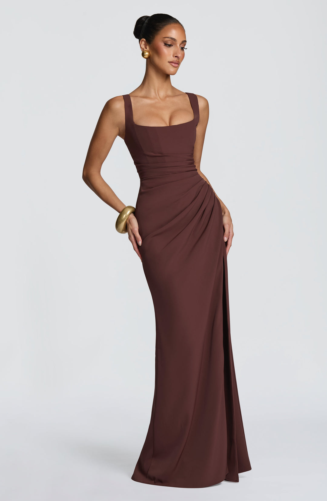 Robe marron chocolat en pose de côté, une main sur la hanche, silhouette ajustée, drapé à la taille et fente latérale. 5
