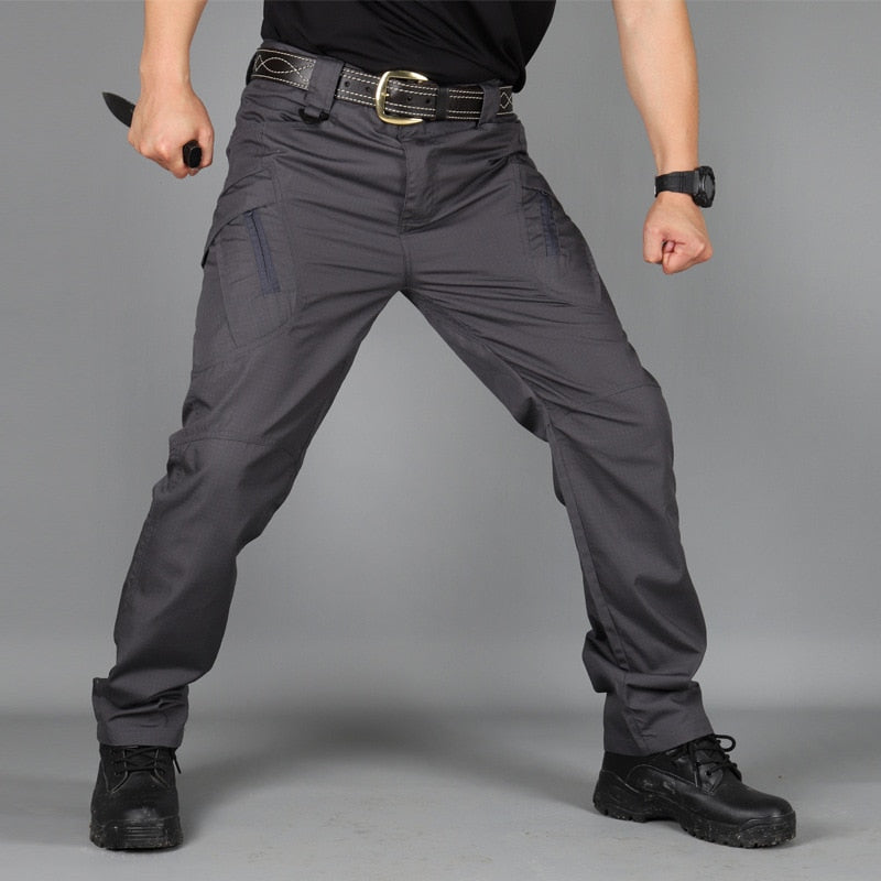 Pantalon gris anthracite porté de face en position de garde, avec poches cargo zippées et ceinture en cuir à boucle dorée. 6