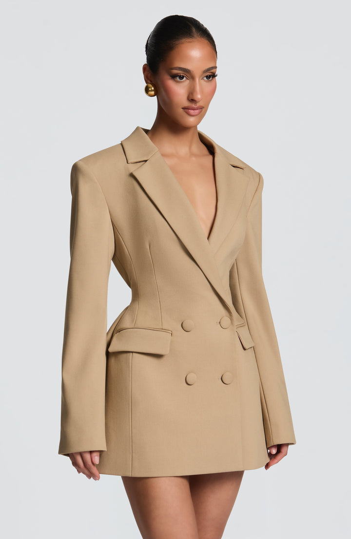 Vue de trois quarts de la robe blazer beige, taille marquée, épaules structurées, poches à rabat et boutons recouverts de tissu. 24