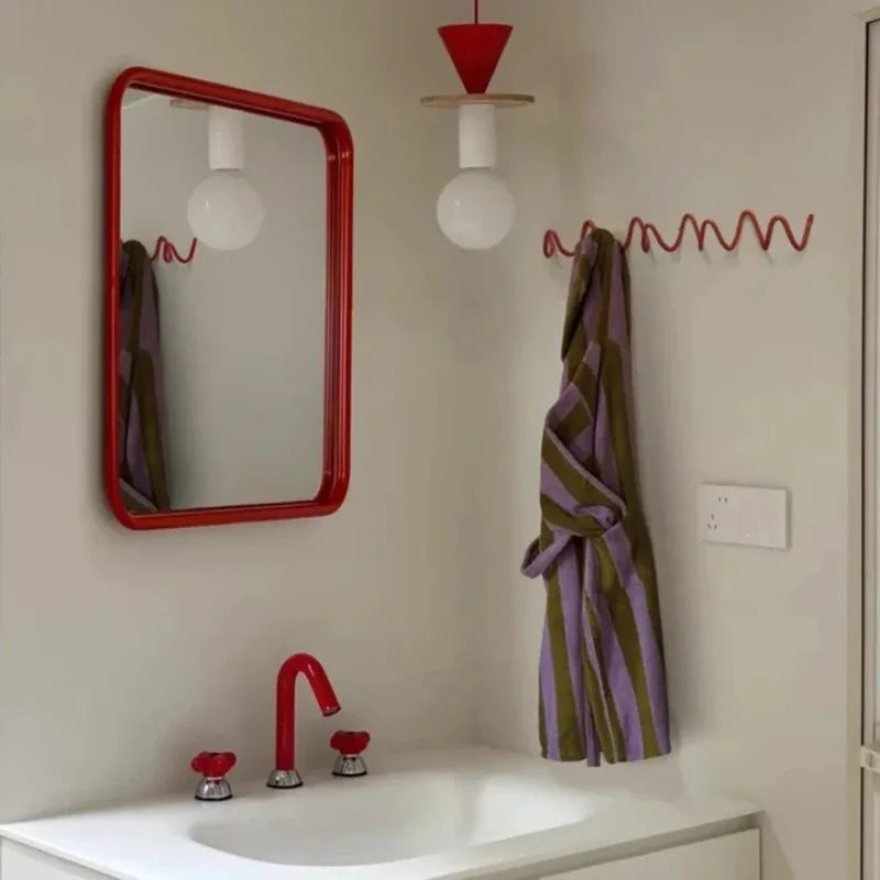 Portant rouge ondulé au mur d'une salle de bains, un peignoir rayé violet et vert accroché, miroir rouge à côté. 2