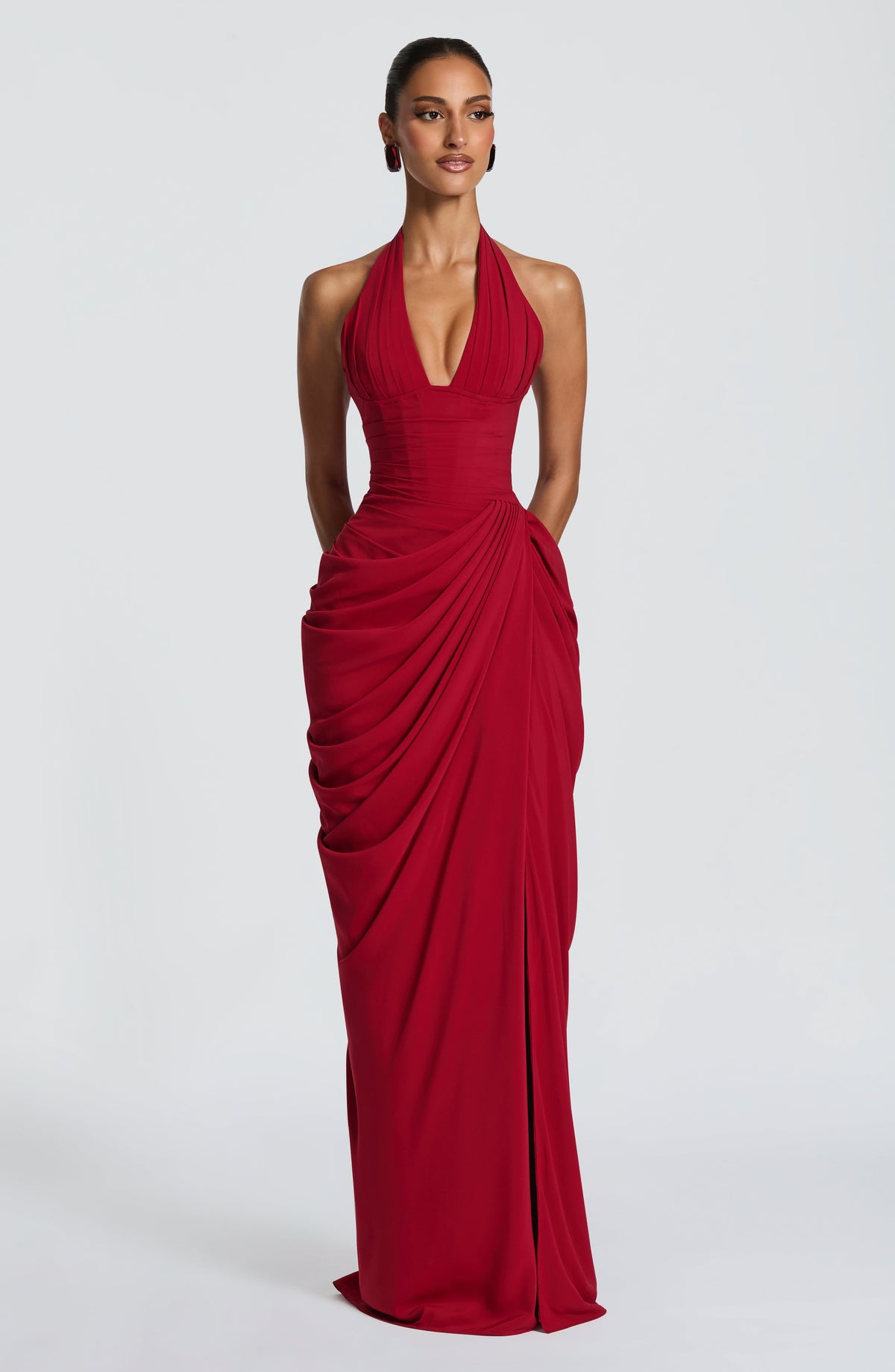 Mannequin de face en robe longue rouge à bustier corseté, décolleté plongeant et jupe drapée, fond de studio gris clair. 21