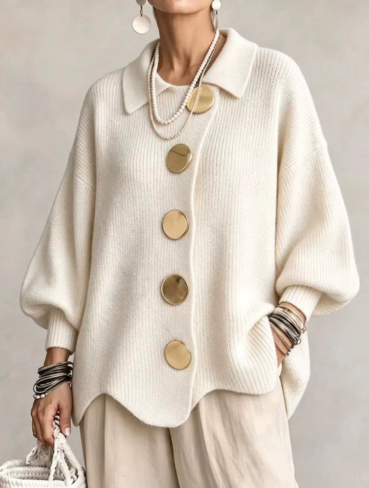 Vue de face du cardigan blanc crème en maille côtelée, grands boutons dorés, porté avec un pantalon beige clair et des colliers de perles. 5