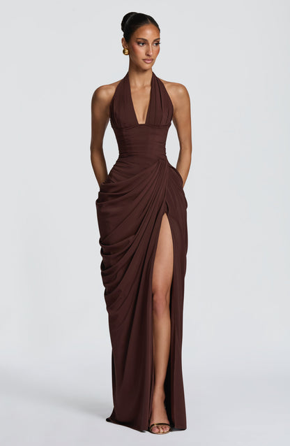 Robe longue marron chocolat portée de face, bustier corseté, jupe drapée sur le côté et haute fente, fond de studio. 24