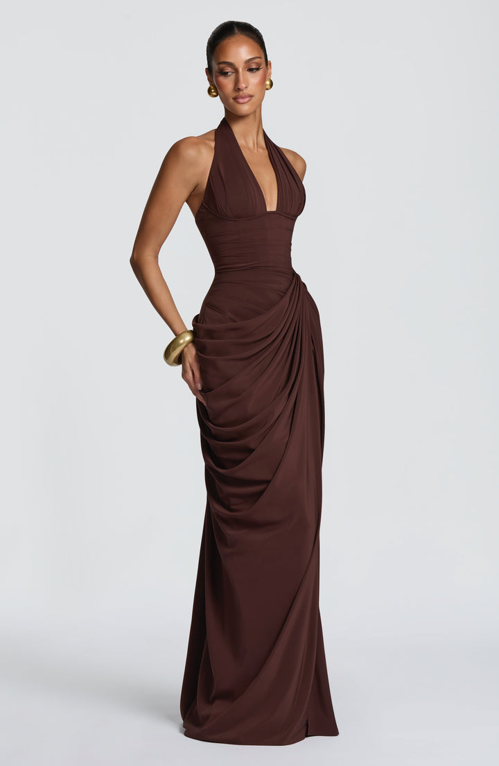 Robe longue marron en trois quarts, mannequin regardant vers le bas, jupe drapée sur la hanche, sans fente apparente. 28